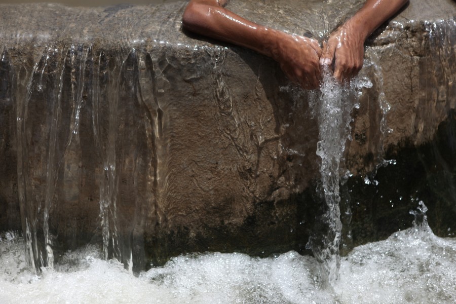 hands funnel water into a chute as it spills over the edge of the falaj in misfat oman